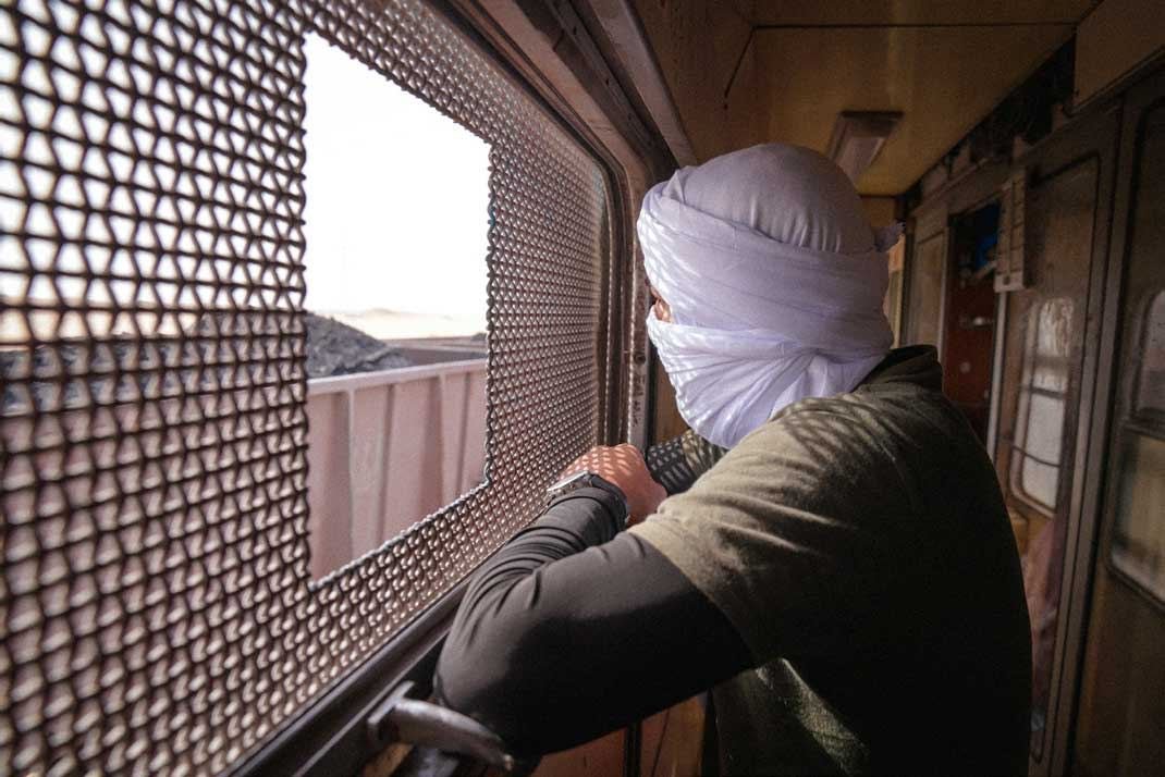 A traveller in a turban looking out of the iron ore train window before Nouadhibou